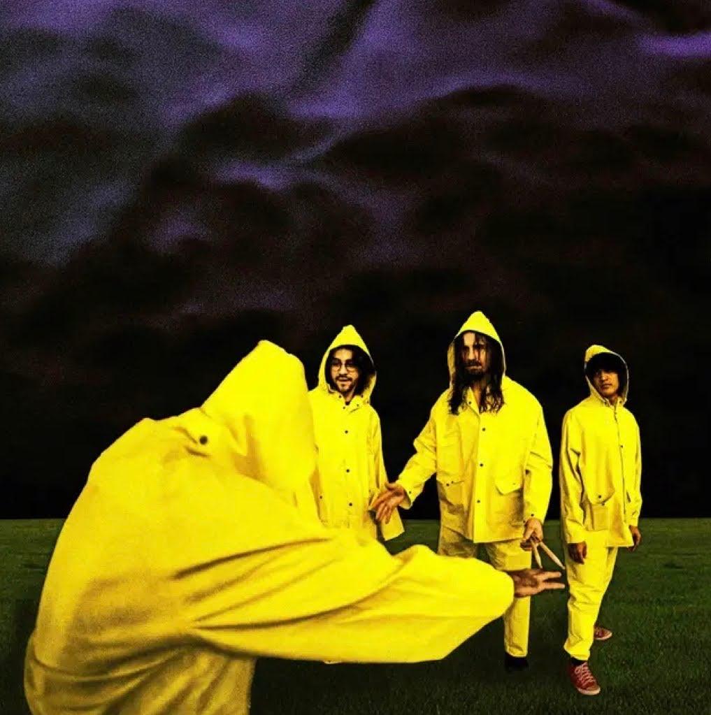 An image of the band in yellow raincoats in a field under a dark sky.